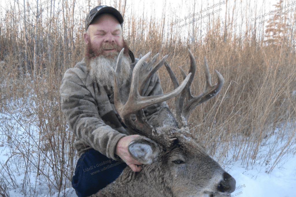 A man with a beard and hat kneeling down with a deer.