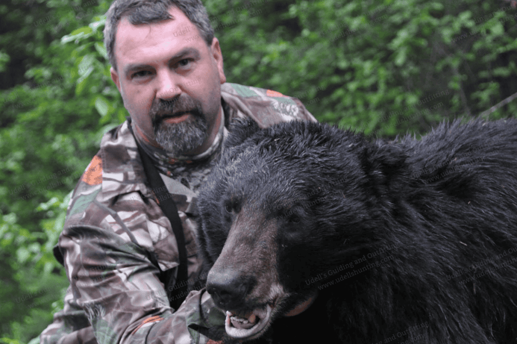 A man holding a black bear in the woods.