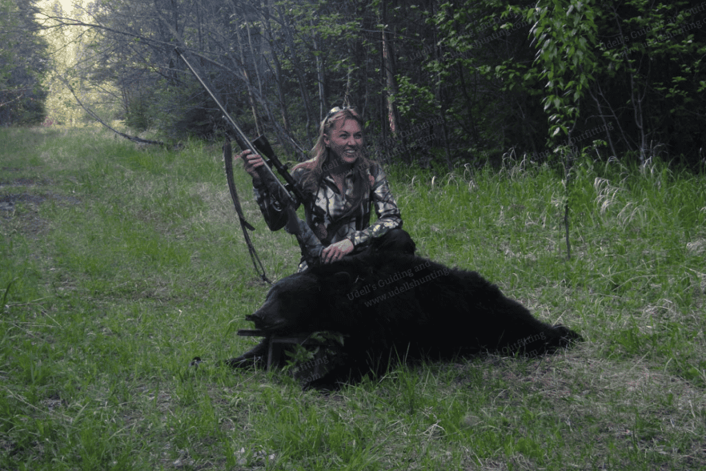 A woman is sitting on the ground with a gun and a bear.