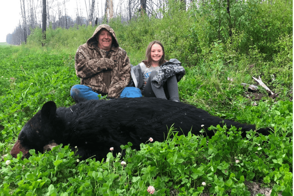 Two people are kneeling next to a black bear.